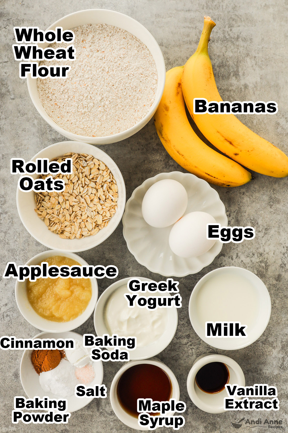 Recipe ingredients including bowls of whole wheat flour, rolled oats, applesauce, greek yogurt, milk, maple syrup, eggs and bananas