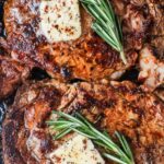 Close up of two ribeye steaks topped with butter and fresh rosemary