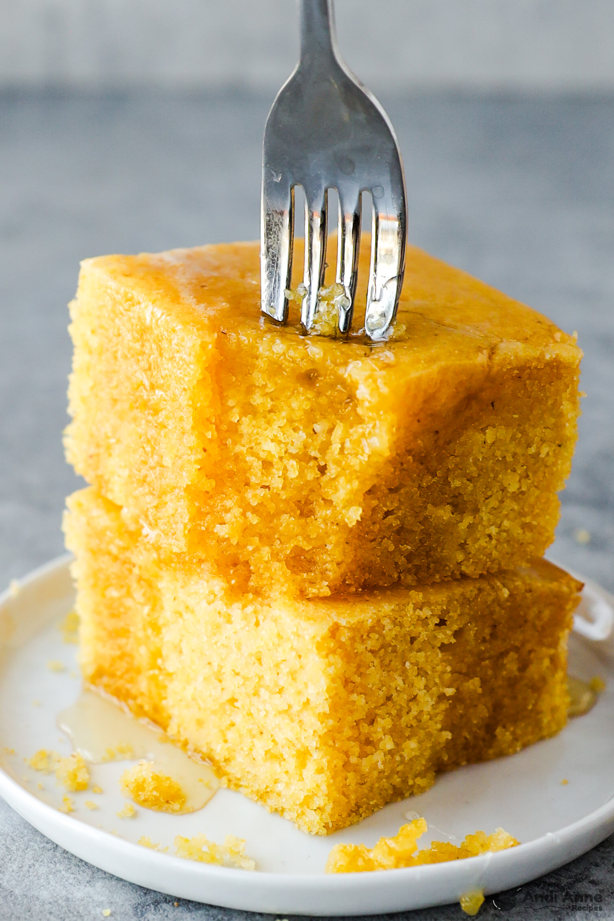 Two pieces of cornbread, drizzled with honey and a fork digging in