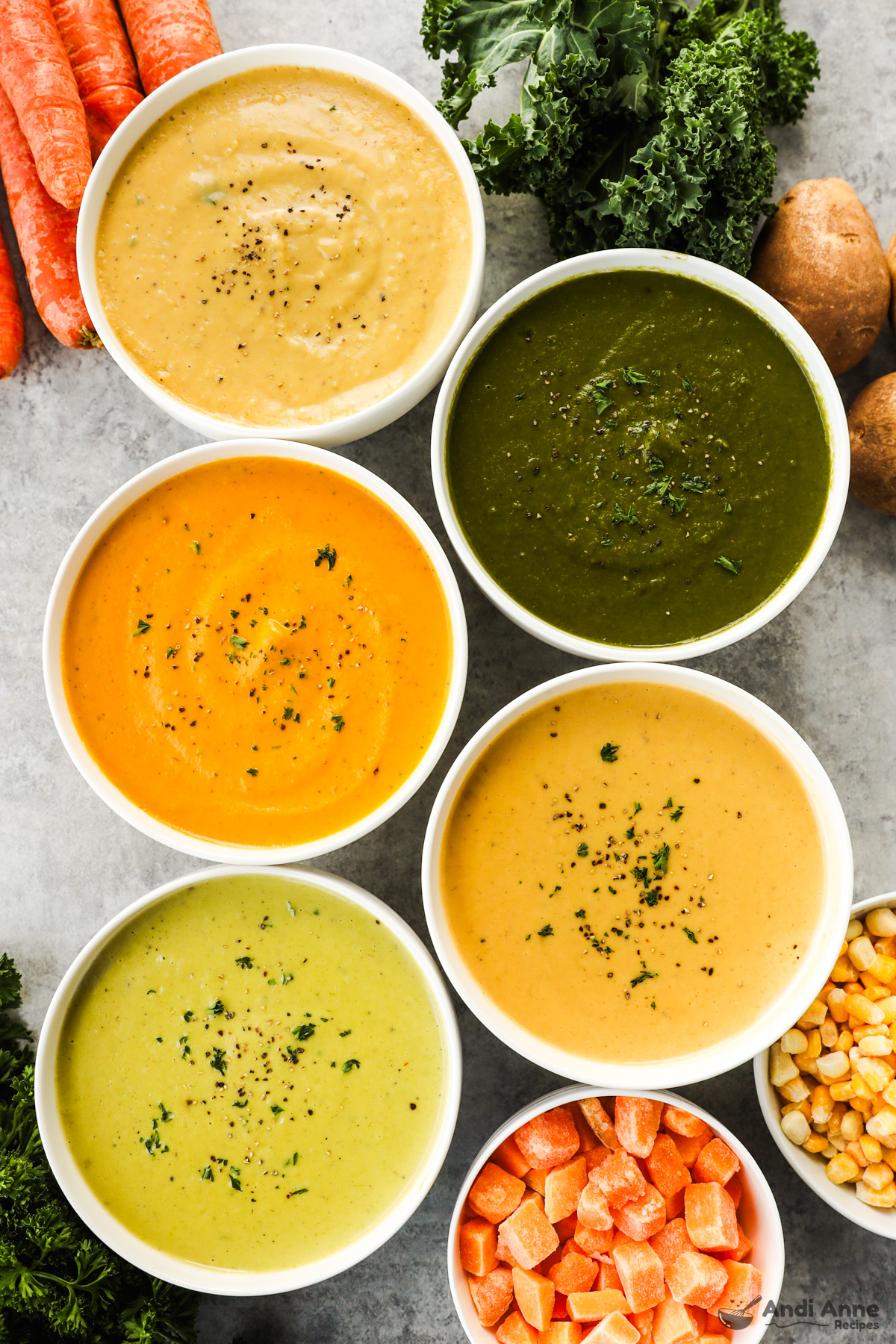 5 bowls of different pureed vegetable soup with vegetables surround the bowls