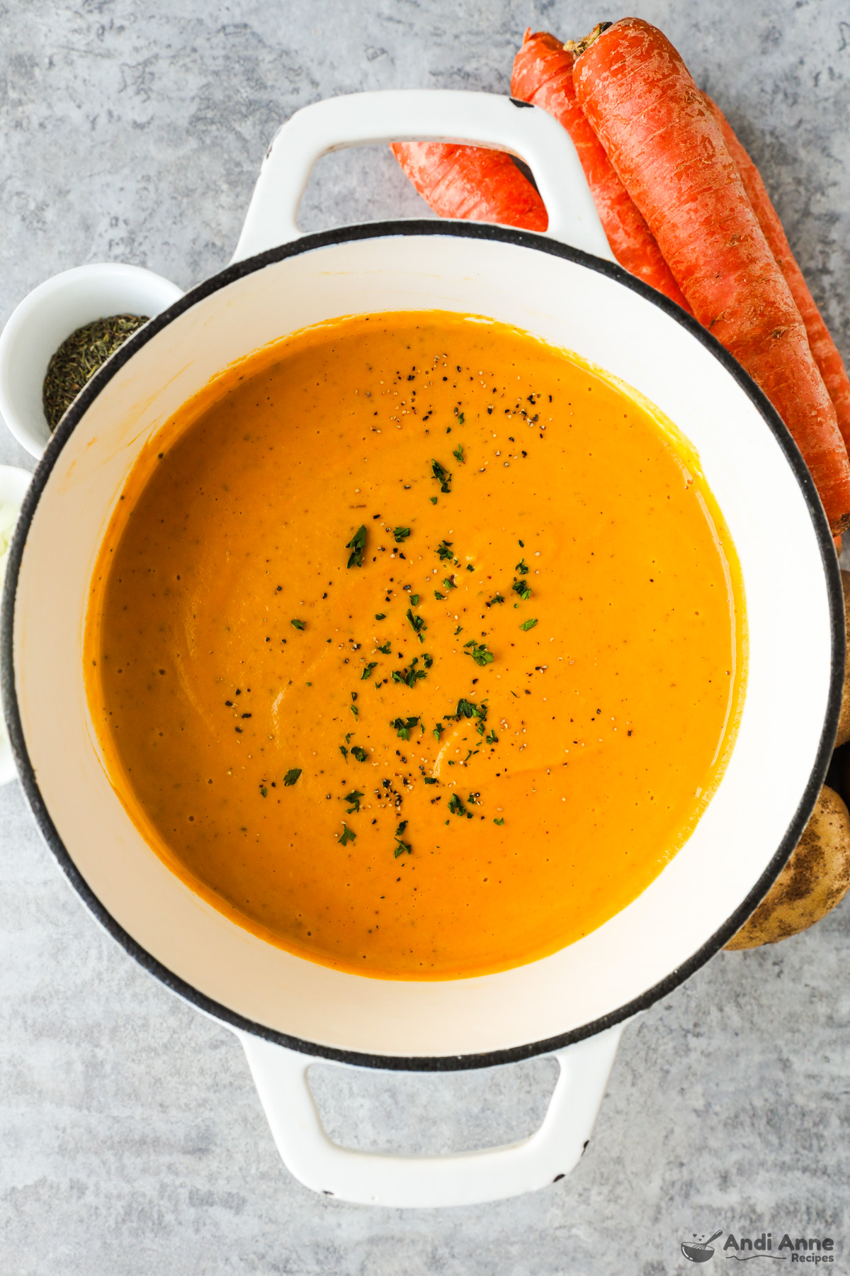 A bowl of creamy carrot soup with some carrots on the side