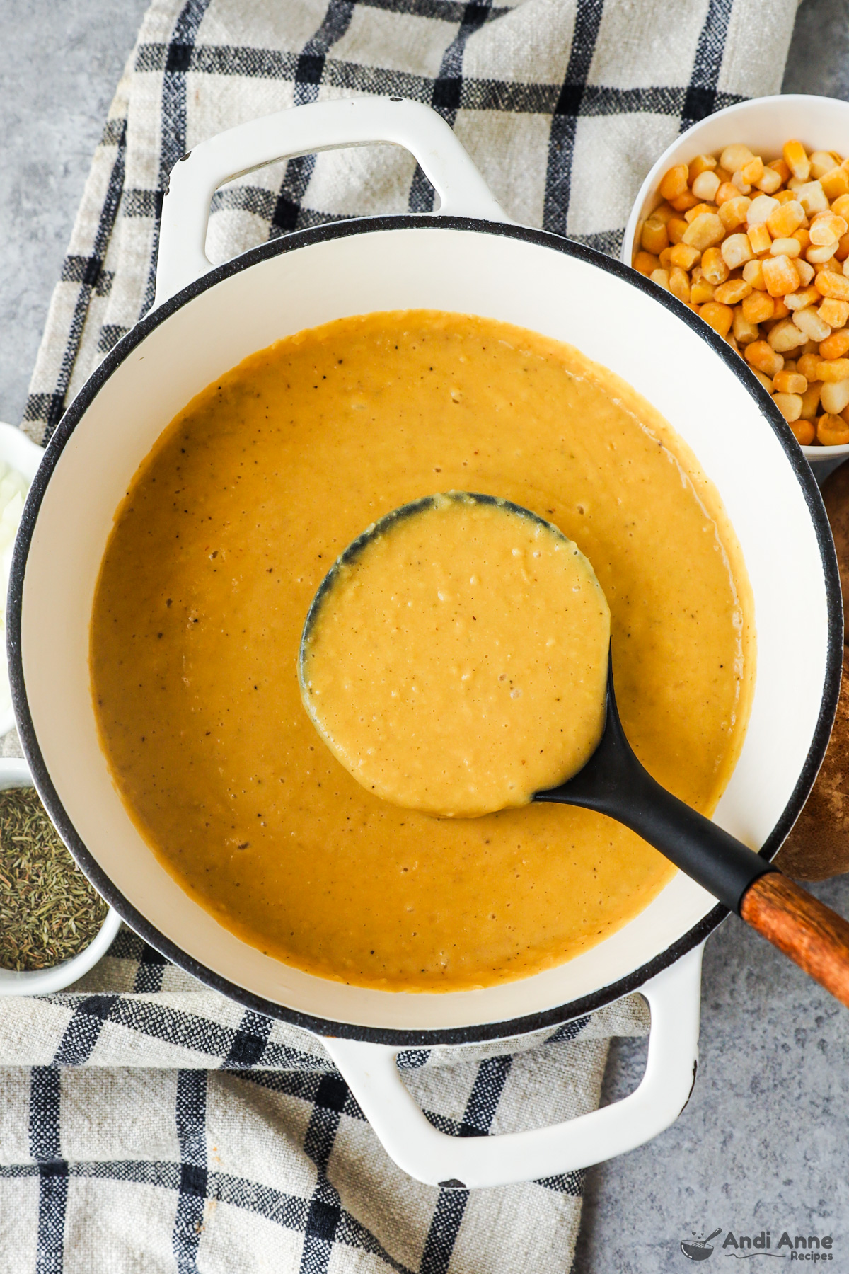 Bowl of creamy corn soup with a soup ladle and bowl of corn on the side