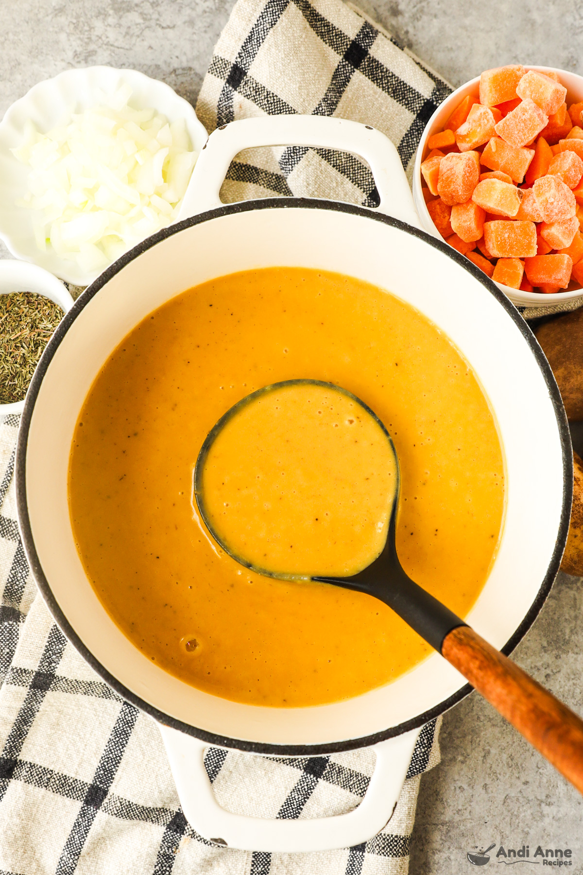 A bowl of creamy butternut squash soup with a soup ladle surrounded with bowls of ingredients