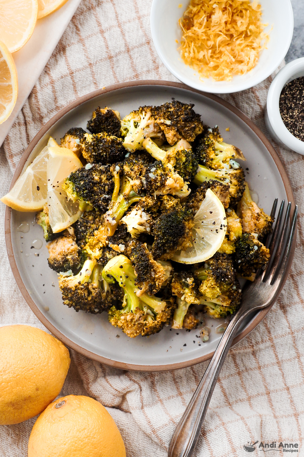 Plate of lemon garlic broccoli with lemon slices, fork and bowls of ingredients surround it