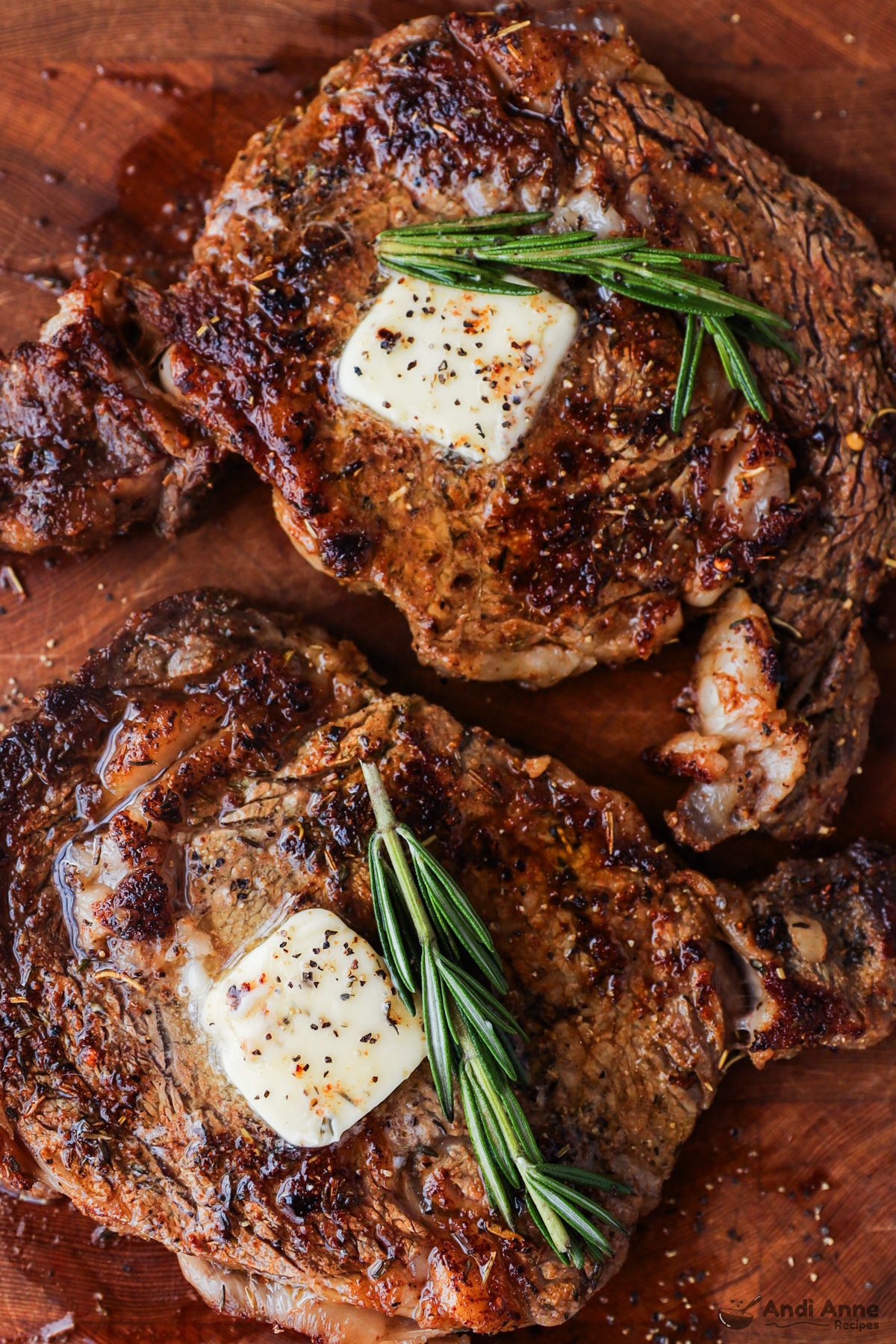 Two cooked steaks with a sprig of rosemary and dollop of butter