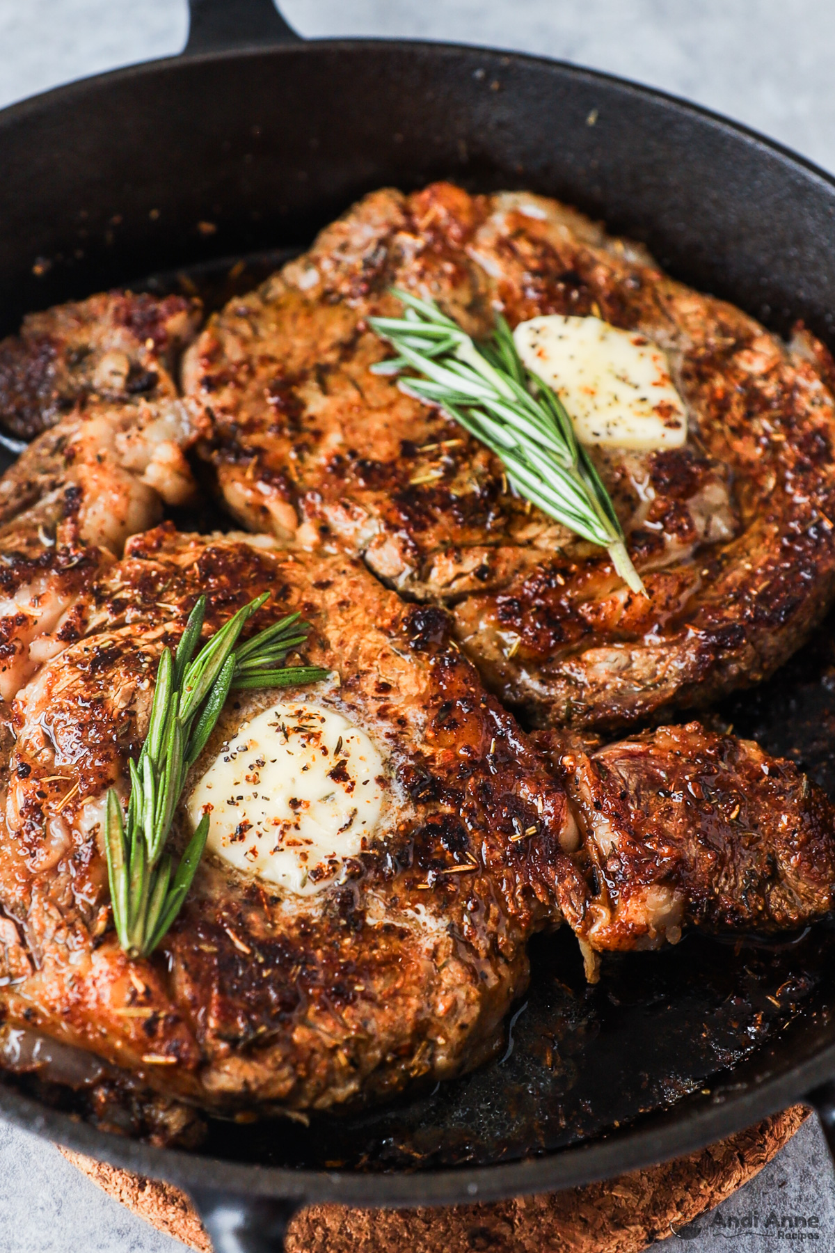 Two steaks in a frying pan with butter and rosemary on top