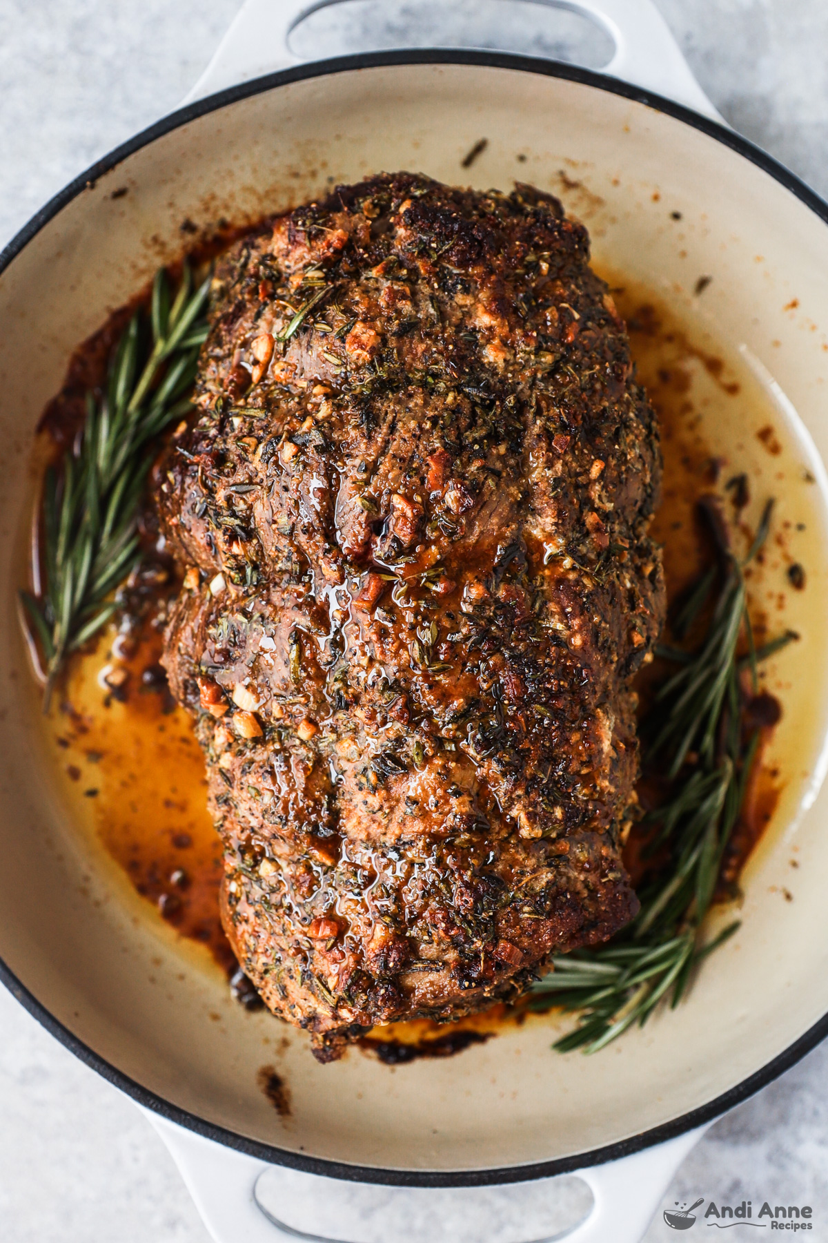 Cooked sirloin tip pot roast in a roasting pan with some fresh rosemary at bottom