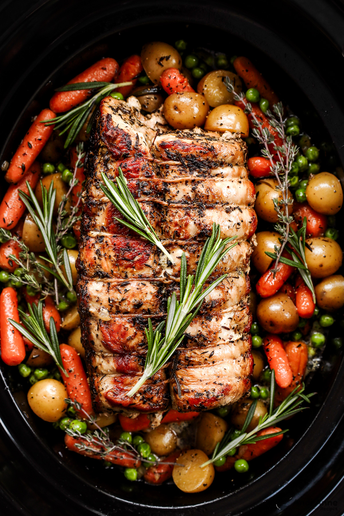 Pork roast in a slow cooker pot with carrots, potatoes and sprigs of rosemary