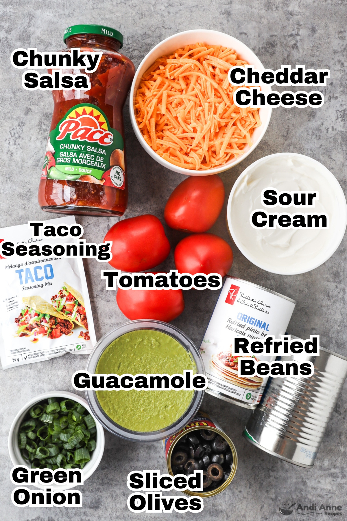 Recipe ingredients including jar of salsa, cheddar cheese, sour cream, roma tomatoes, taco seasoning, guacamole, cans of refried beans, canned olives and chopped green onion