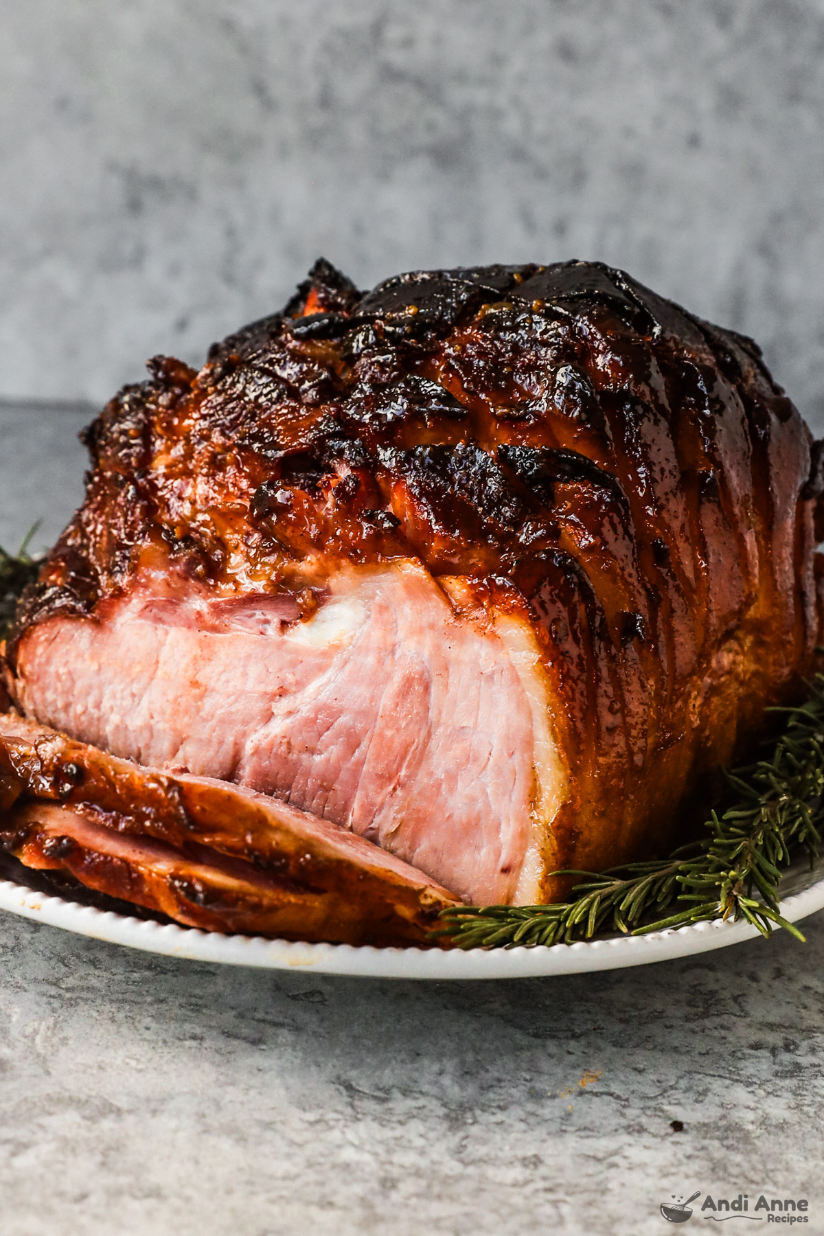 Slices of glazed ham with the whole hame all on a plate with sprigs of rosemary