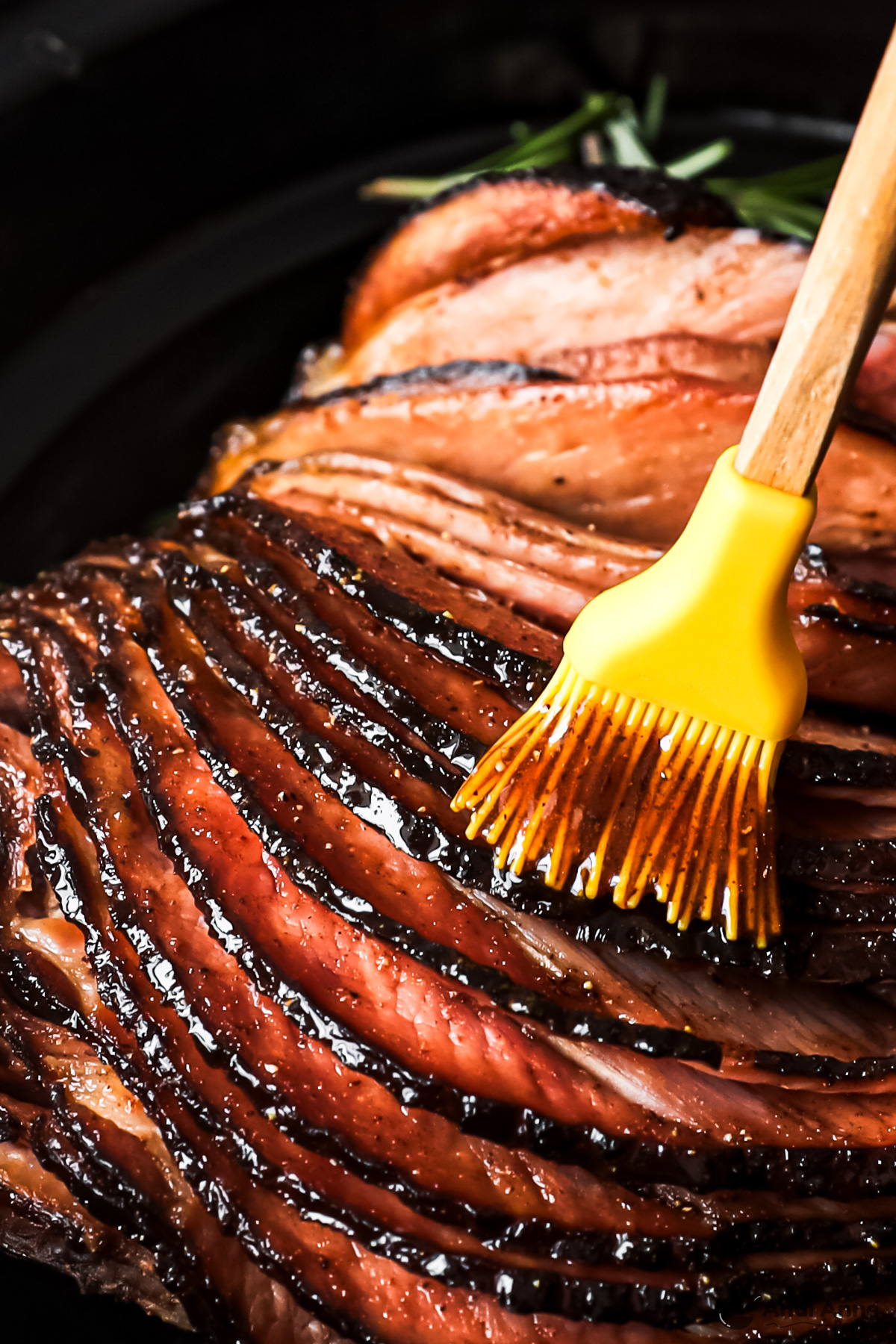 A slow cooker brown sugar glazed ham with a silicone brush spreading the sauce over the ham