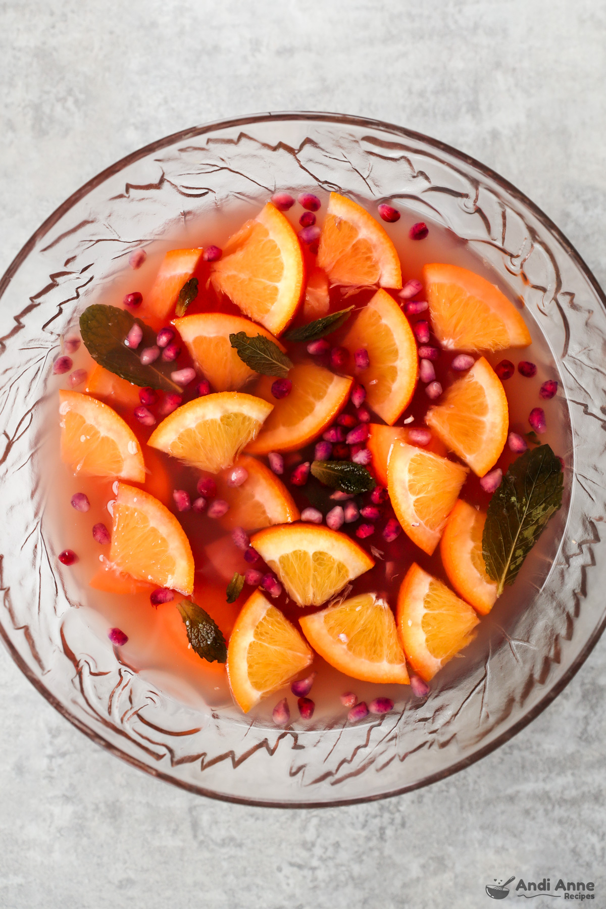 A bowl of punch with orange slices, pomegranate seeds and mint leaves