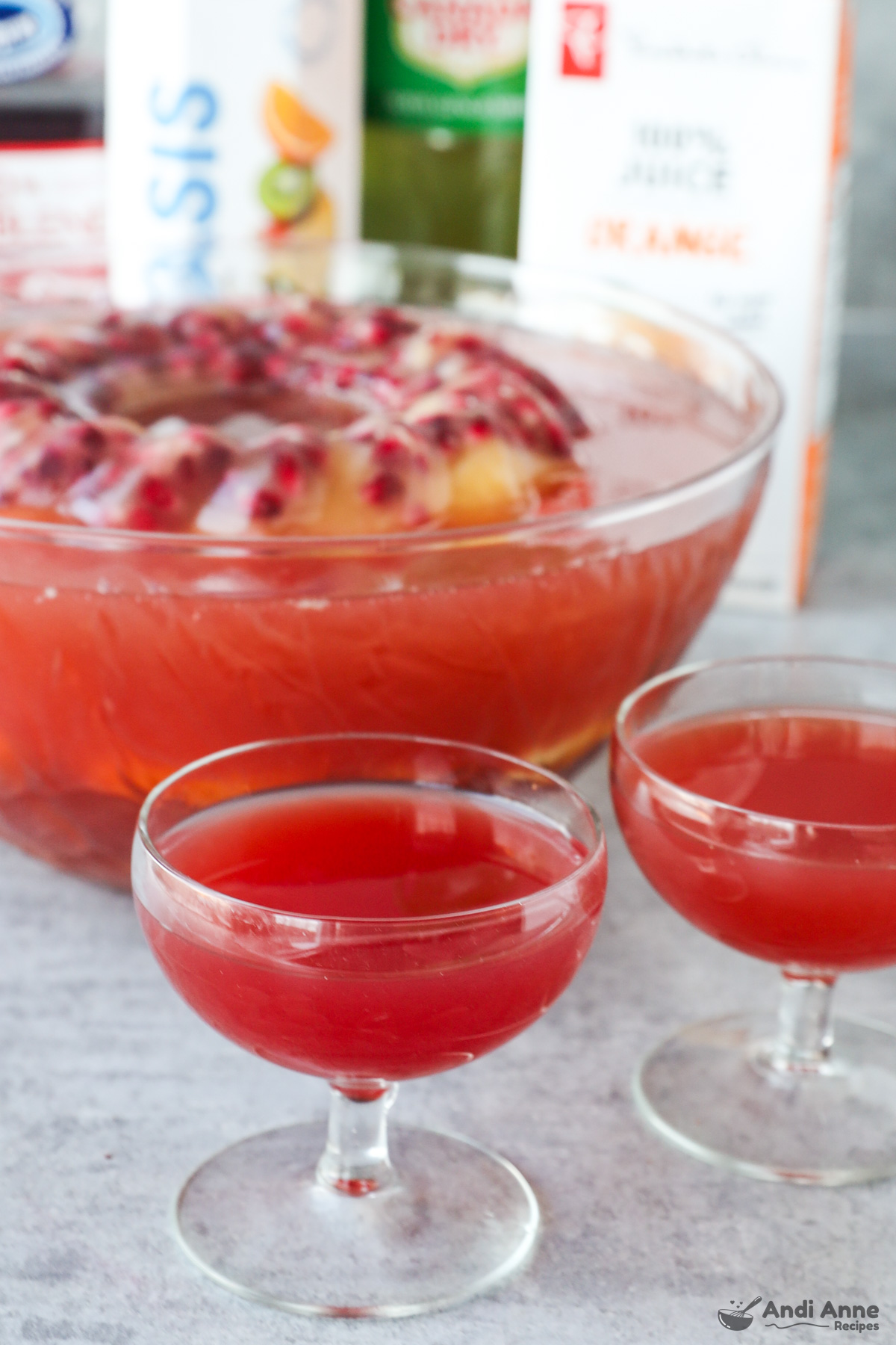 Two glasses of punch with a punch bowl in the background along with containers of juice