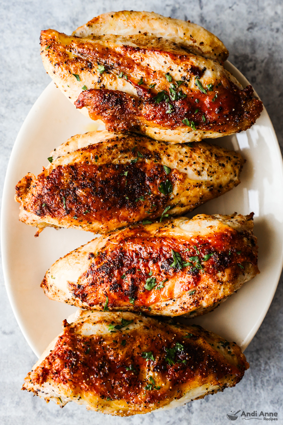 Four crispy bone-in skin-on chicken breasts on a plate.