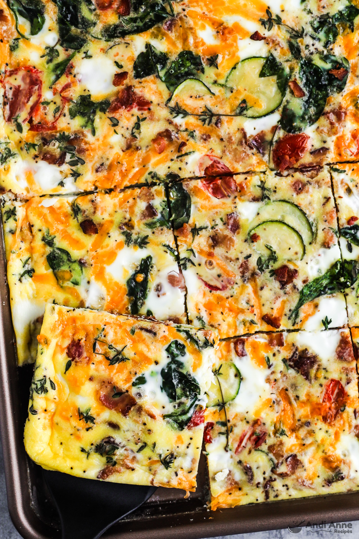 Close up of the cut sheet pan frittata slices loaded with veggies, cheese and bacon but still on the baking sheet