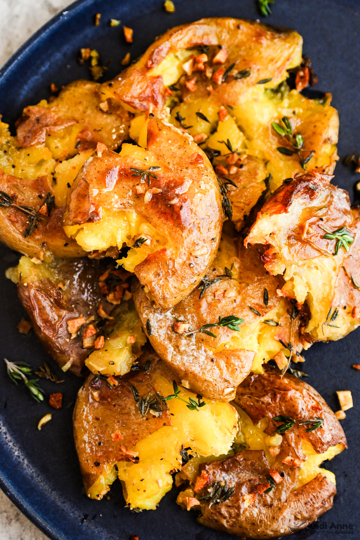 A plate of crispy smashed potatoes close up with crispy garlic and thyme