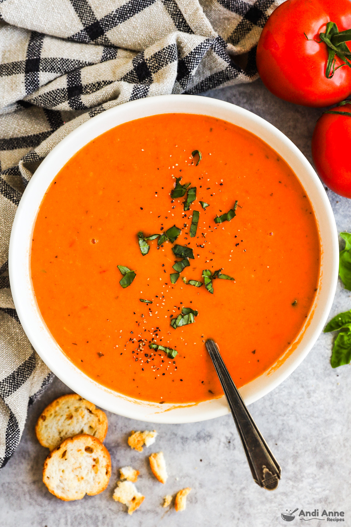 bowl of tomato soup with spoon and chopped basil on top