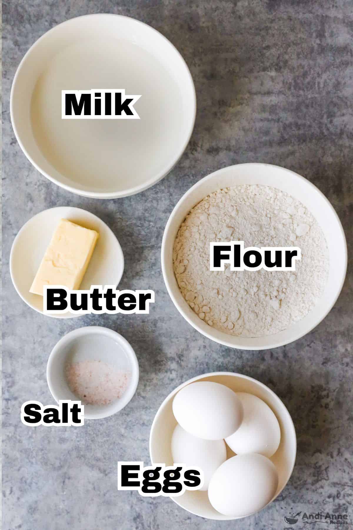 Recipe ingredients in bowls including milk, flour, butter, salt and eggs