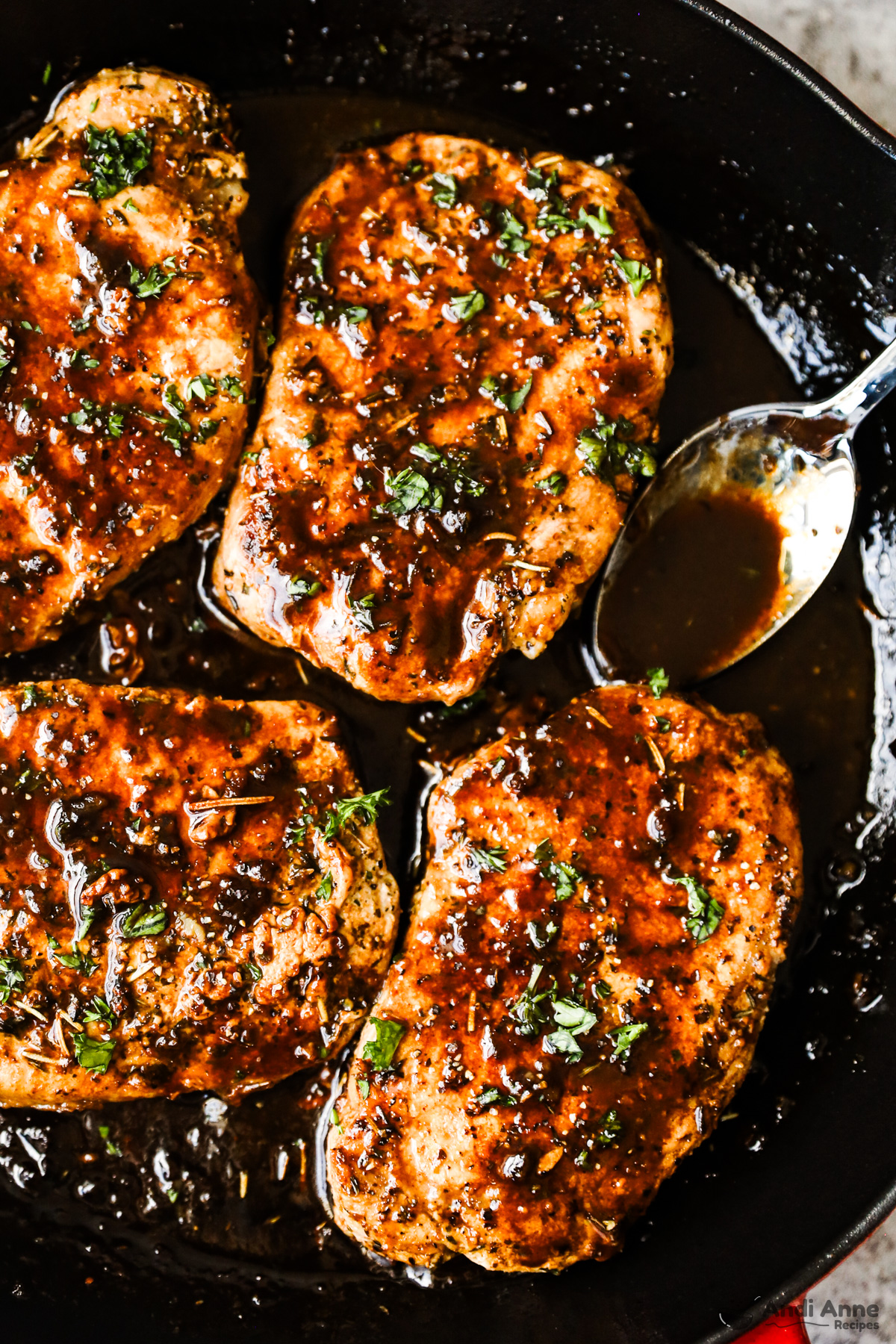 Balsamic glazed pork chops coated in brown sauce, with a spoon beside and a sprinkle of chopped parmesan