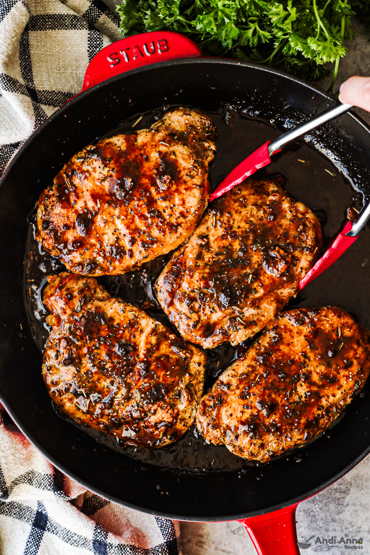 Pork chops in skillet with balsamic sauce drizzled on top and tongs holding pork chops