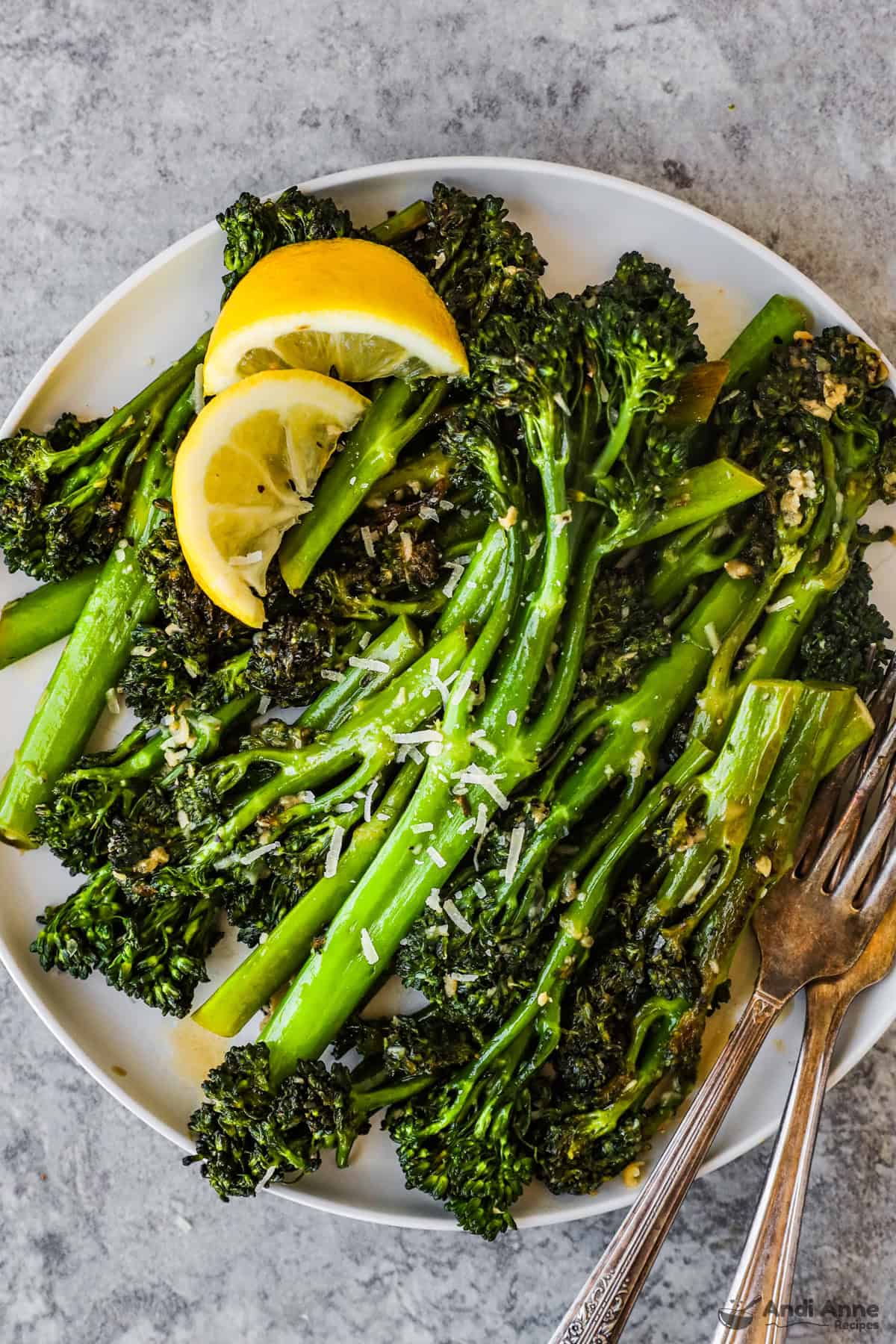 Plate with broccolini, lemon slices, forks and sprinkle of parmesan cheese