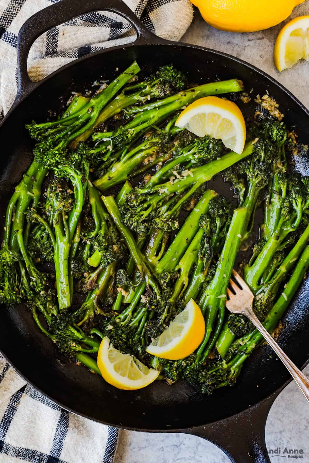 Sauteed broccolini in a skillet with a fork and a couple slices of lemon