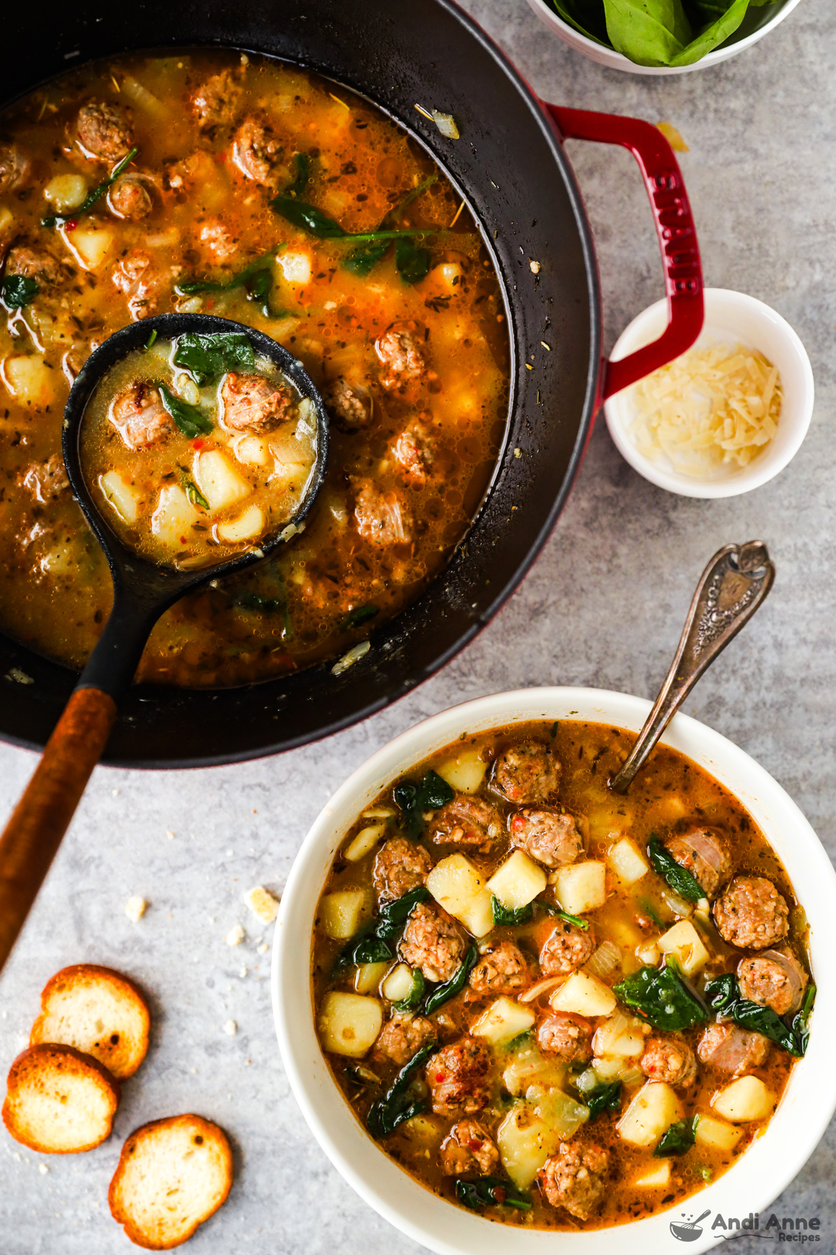 Pot of sausage potato soup with a soup ladle, and a bowl of sausage potato soup with a few crackers beside bowl