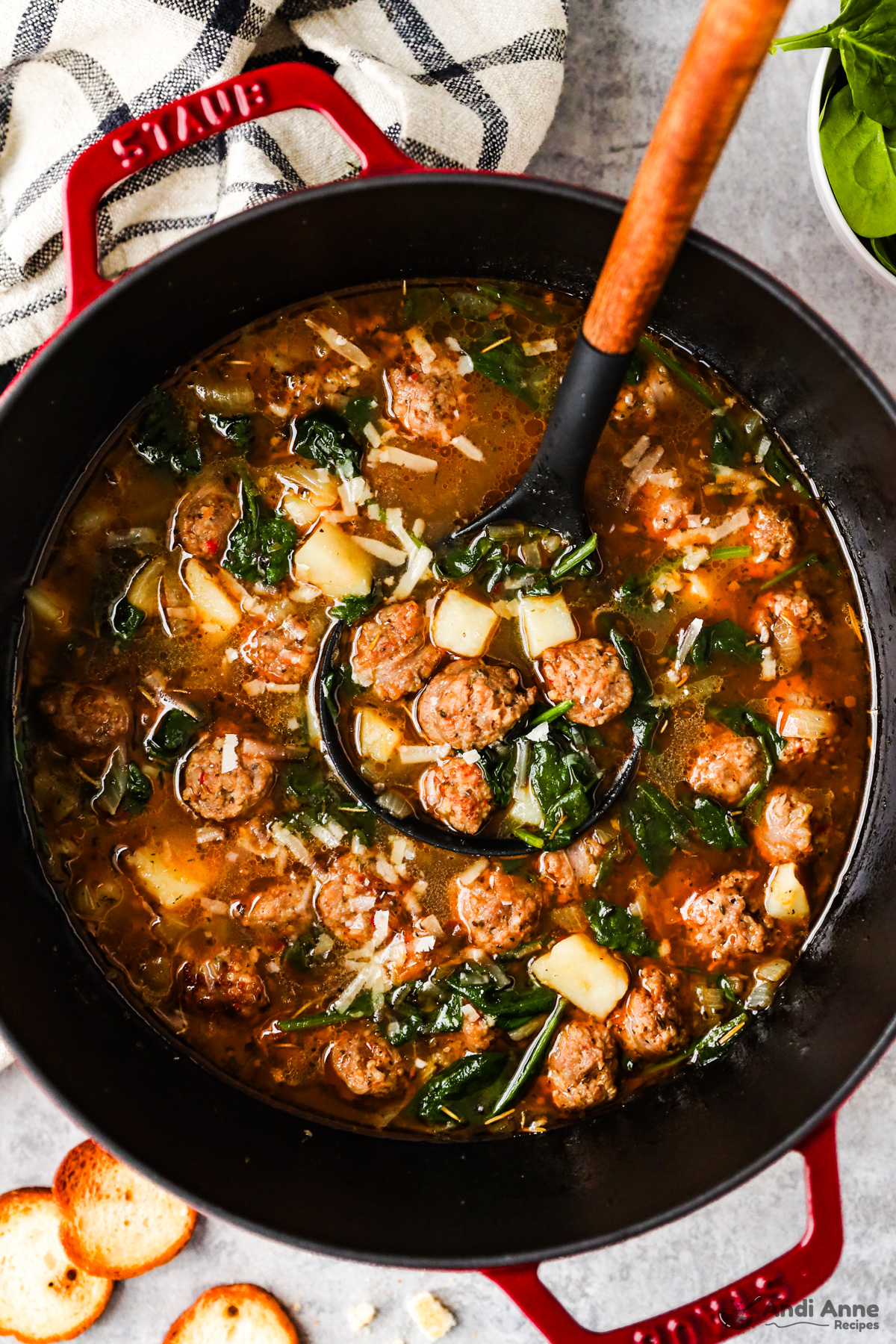 A pot of sausage potato soup with a soup ladle