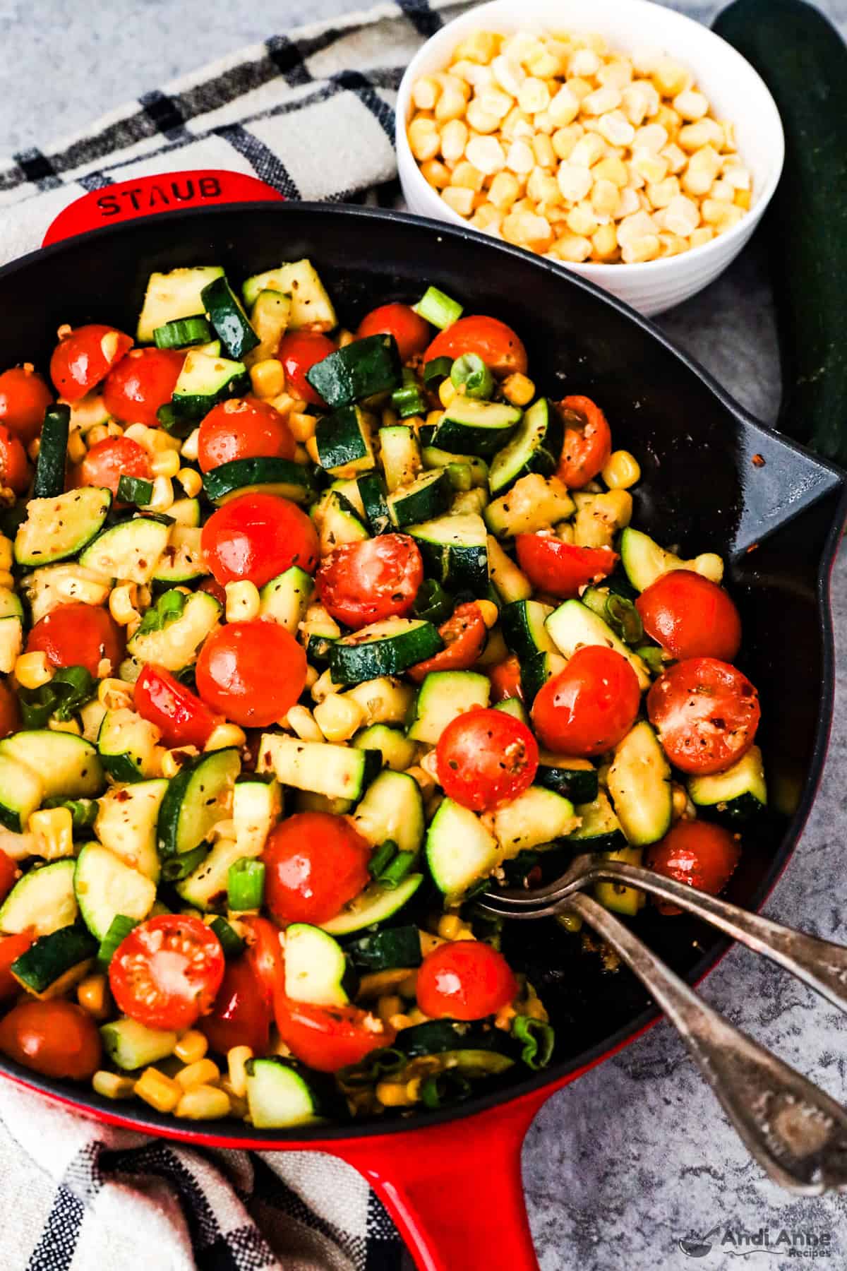 A skillet with chopped zucchini, tomatoes, corn and green onion