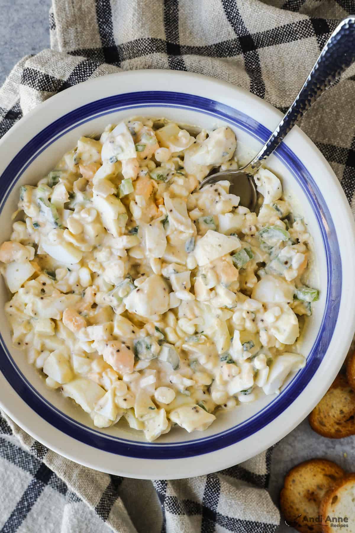 Overhead view of finished egg salad in a bowl with a spoon and crackers on the side. 