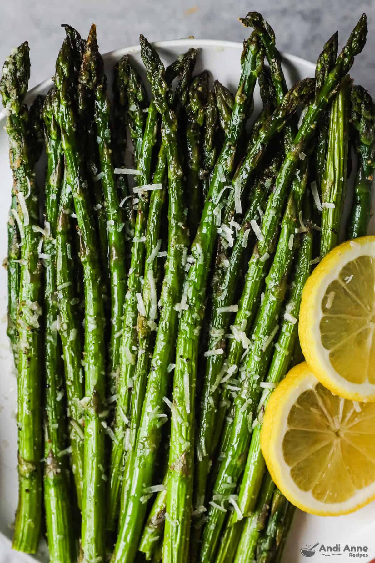 Closeup image of cooked asparagus with grated parmesan cheese and two lemon slices. 