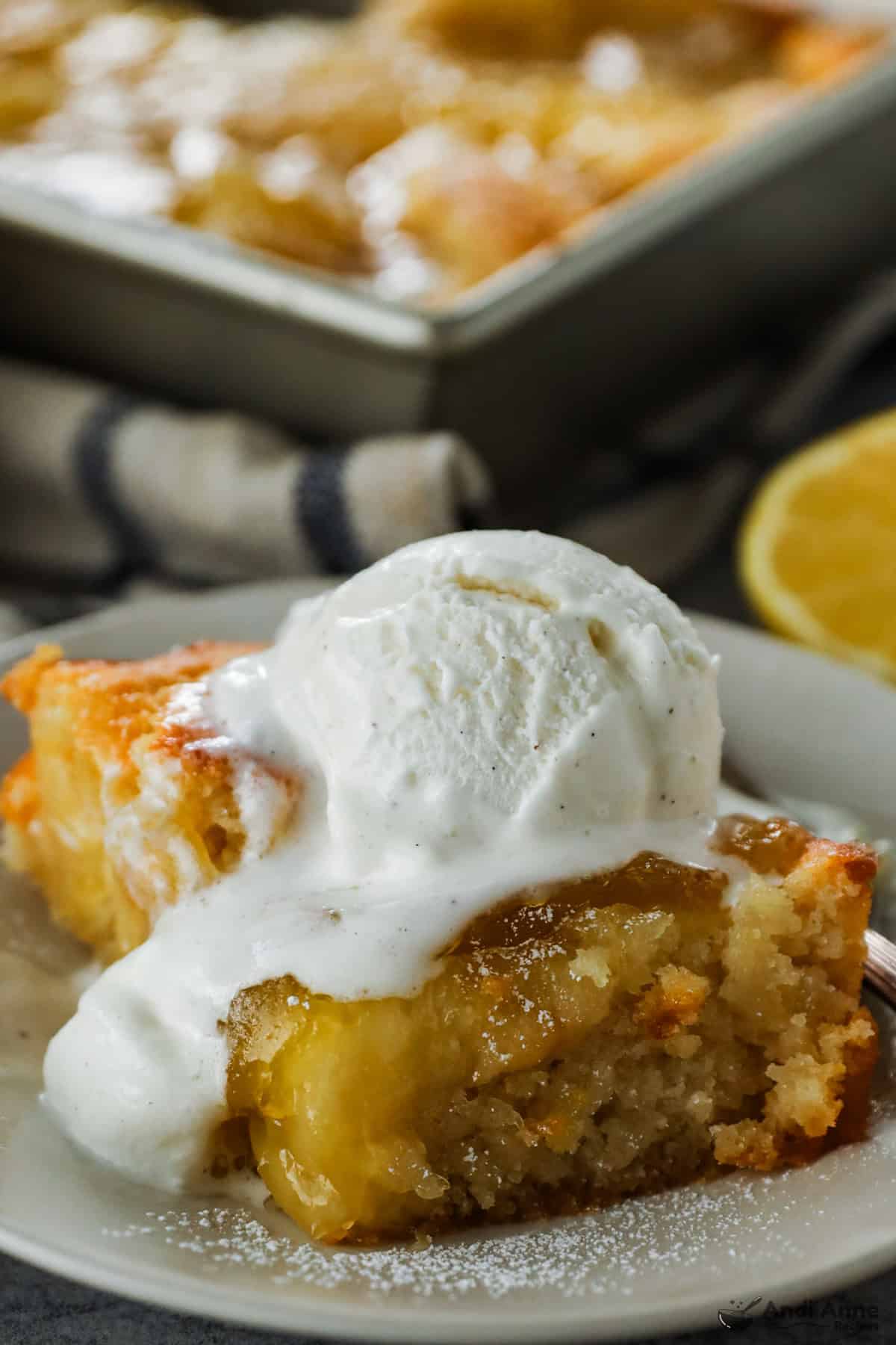 A slice of magic lemon cobbler topped with a scoop of ice cream on a plate.
