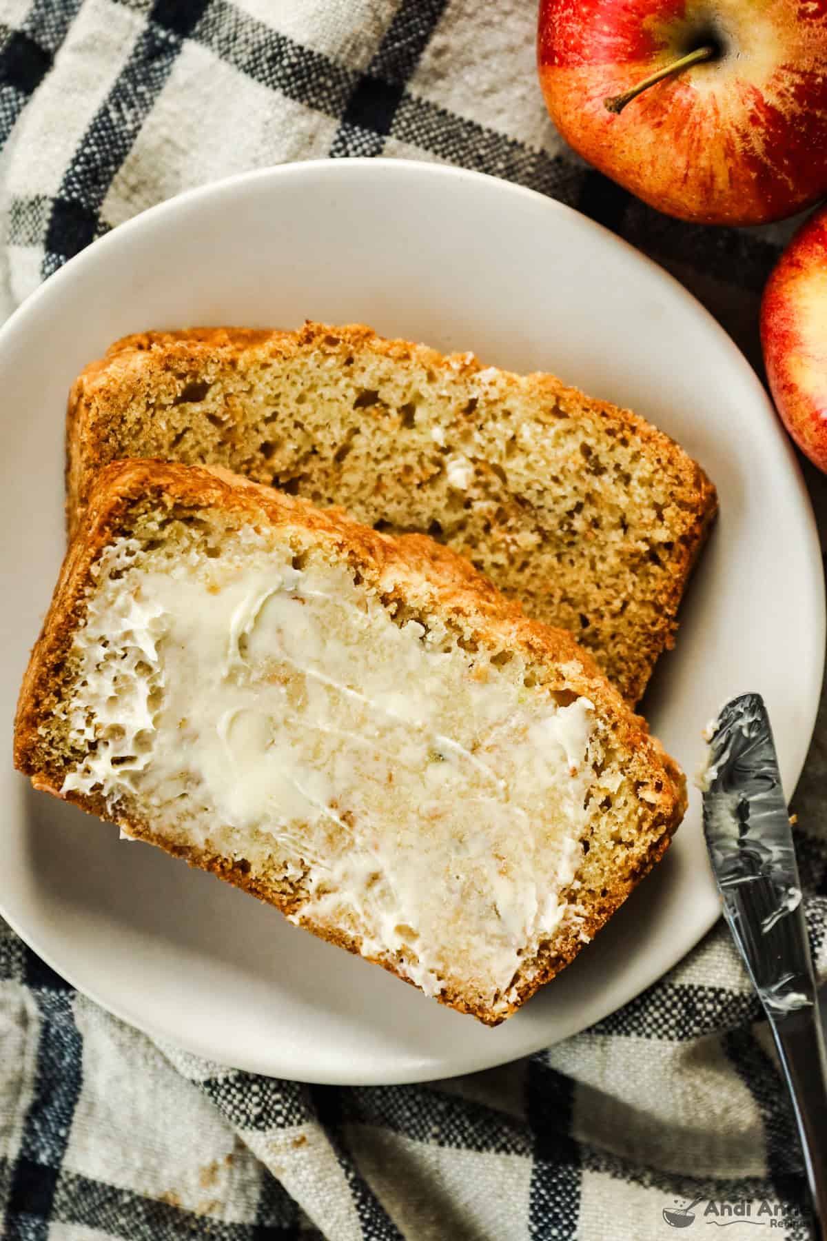 Two slices of apple bread on a plate, the top slice is smeared with butter.
