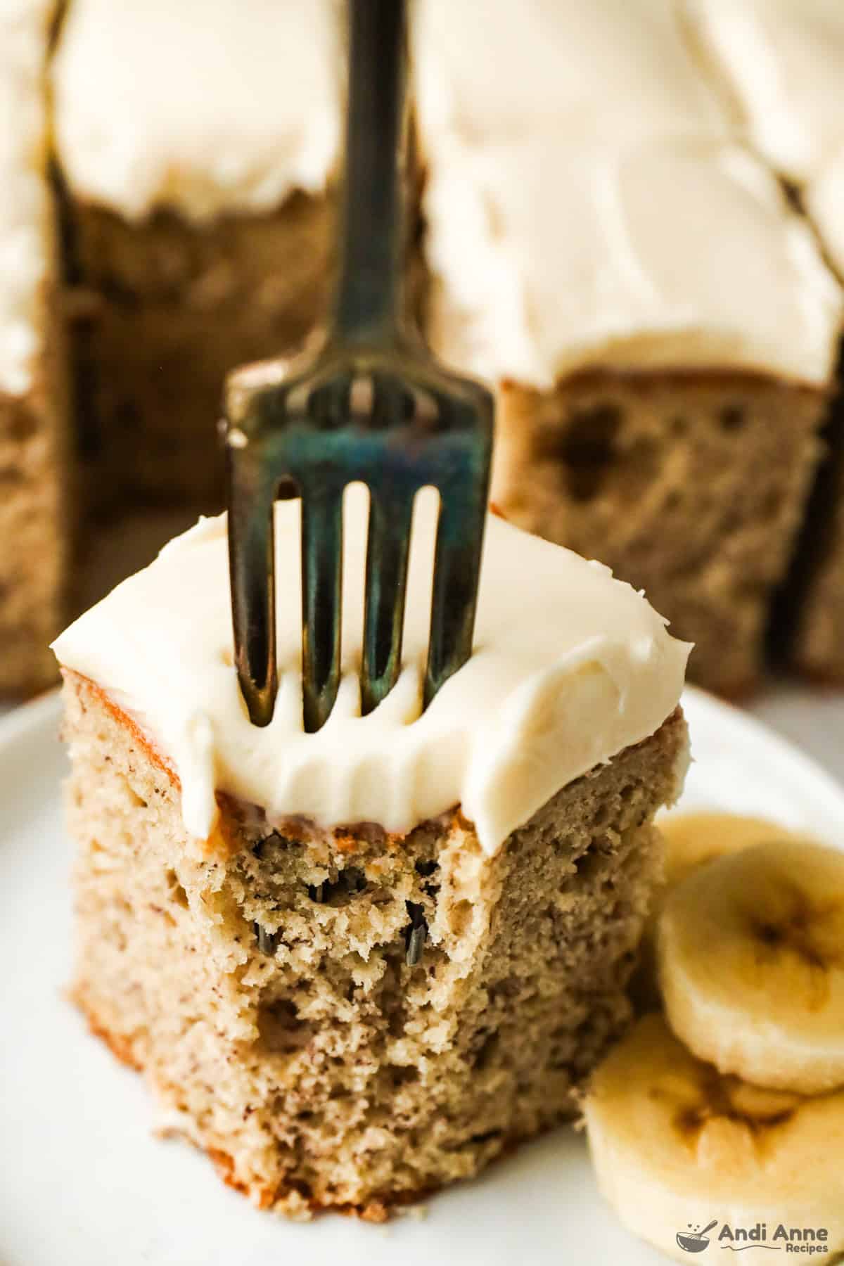 A close-up slice of banana cake with a fork, removing a bite.