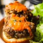 Two cheeseburger tarts on a plate and a side of salad.