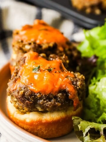 Two cheeseburger tarts on a plate and a side of salad.