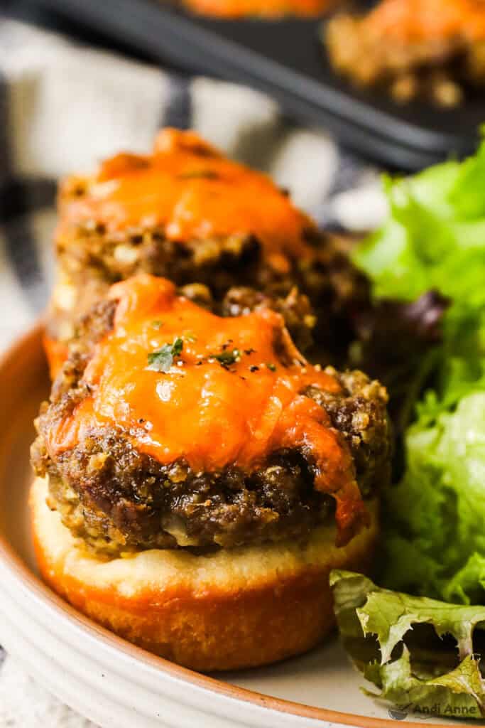Two cheeseburger tarts on a plate and a side of salad.