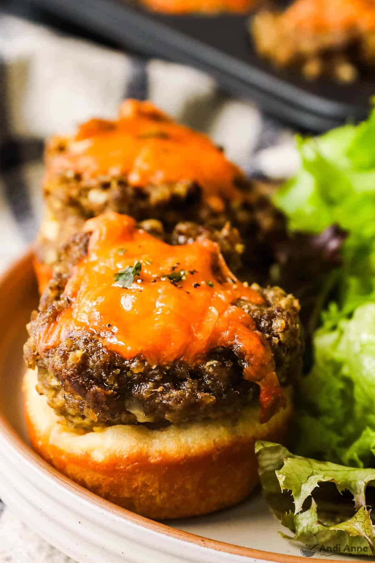 Two cheeseburger tarts on a plate and a side of salad.