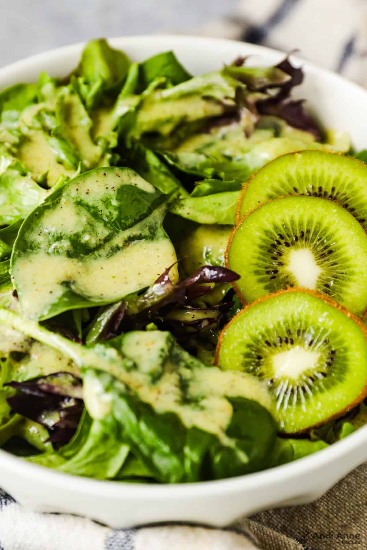 A mixed salad with slices of kiwi is dressed with the dressing.
