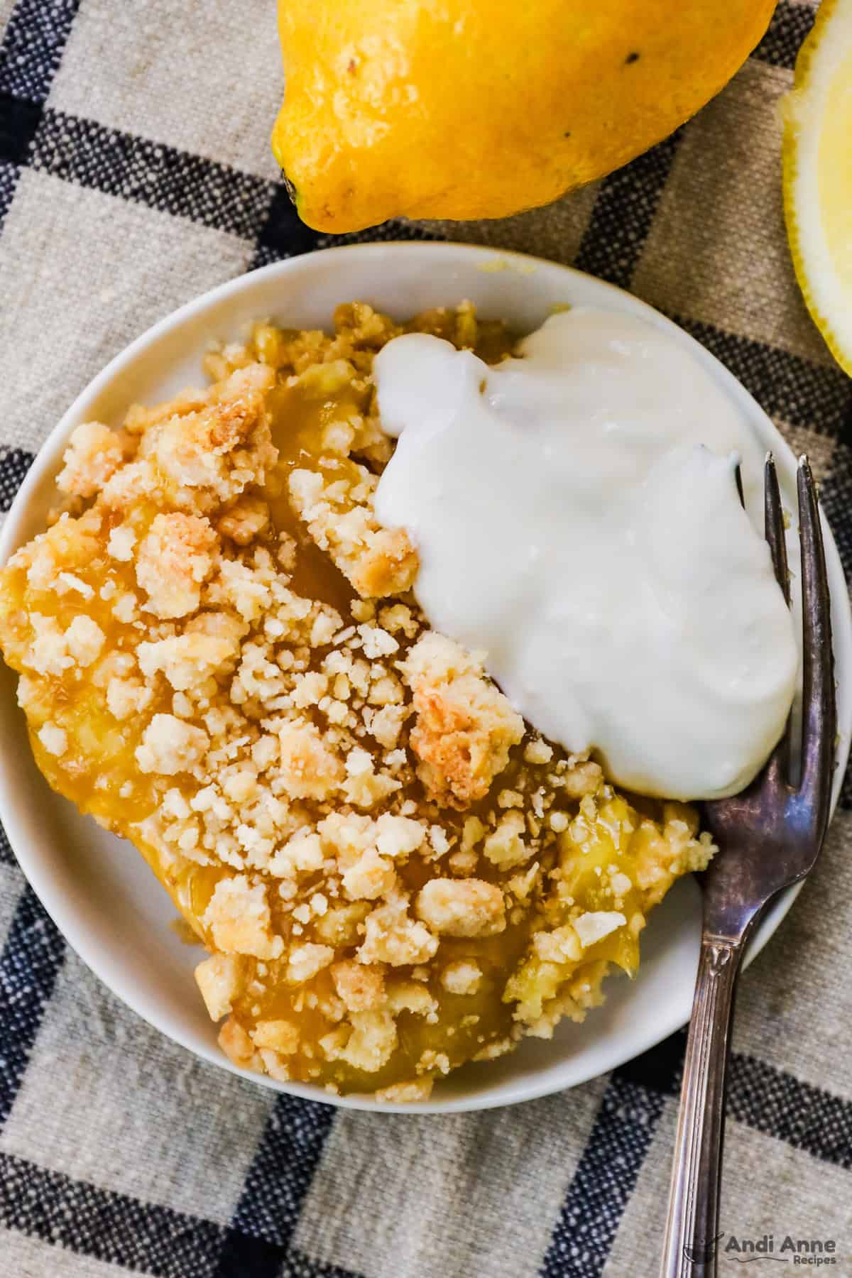 A slice of lemon bar is served on a plate with a dollop of yogurt.