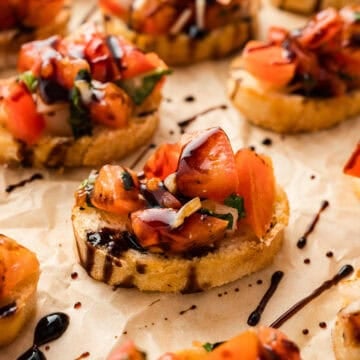 Small slices of toasted baguette topped with tomato bruschetta and balsamic glaze.