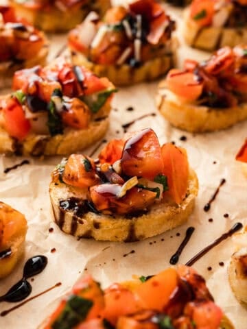 Small slices of toasted baguette topped with tomato bruschetta and balsamic glaze.