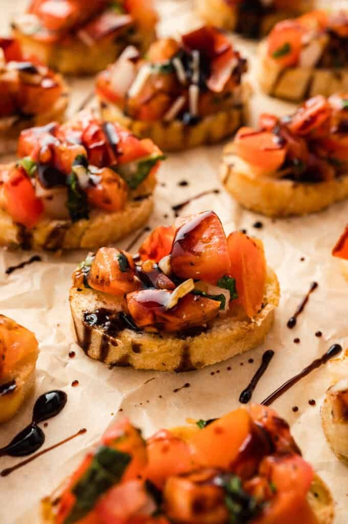 Small slices of toasted baguette topped with tomato bruschetta and balsamic glaze.