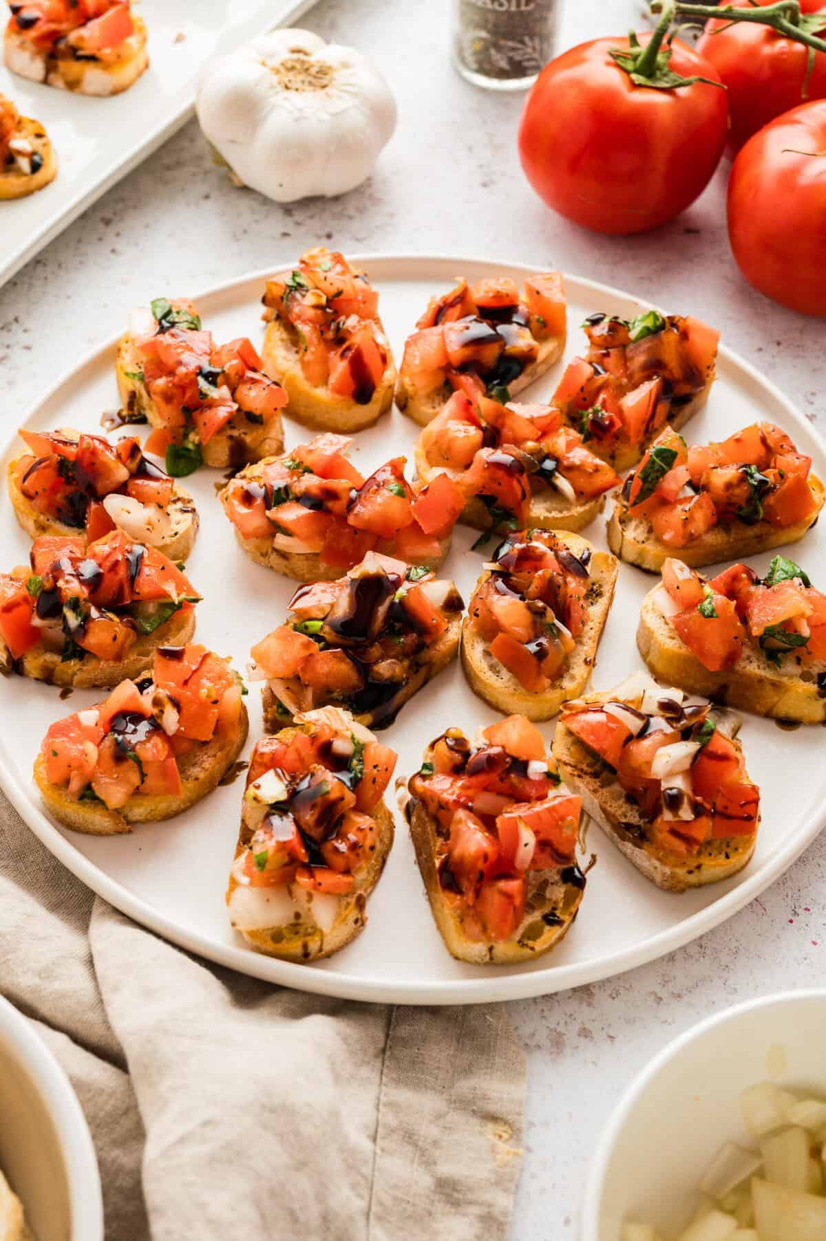 Slices of baguette topped with tomato bruschetta are arranged on a white plate.