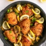 Artichoke chicken in a skillet with lemon slices.