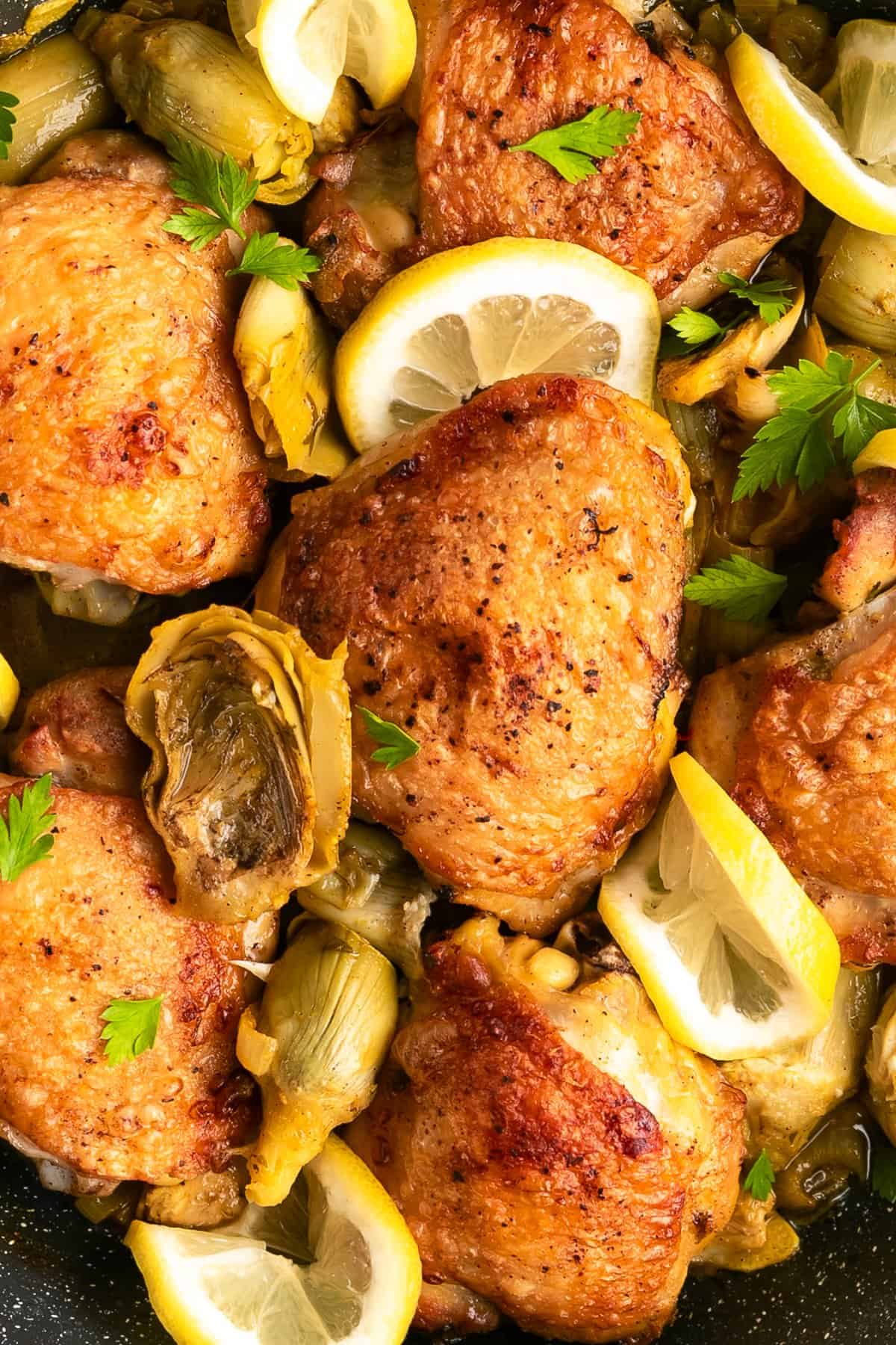 Crispy chicken thighs, artichoke hearts, and lemon in a skillet.