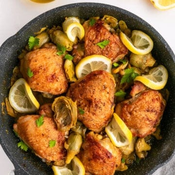 Artichoke chicken in a skillet with lemon slices.