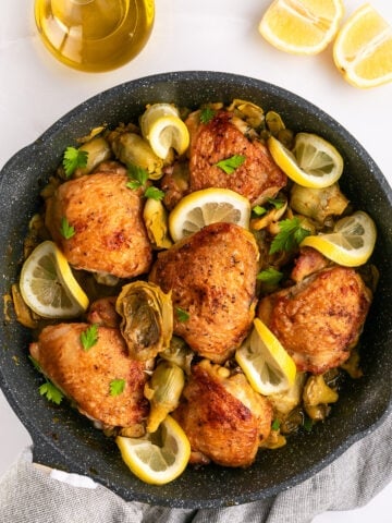 Artichoke chicken in a skillet with lemon slices.