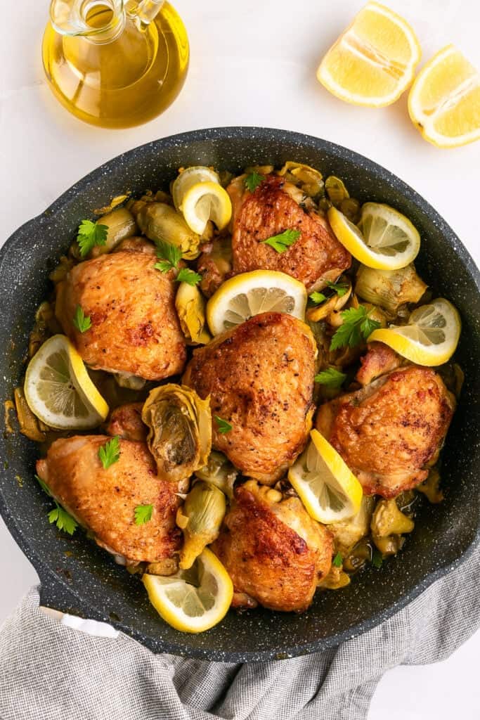 Artichoke chicken in a skillet with lemon slices.