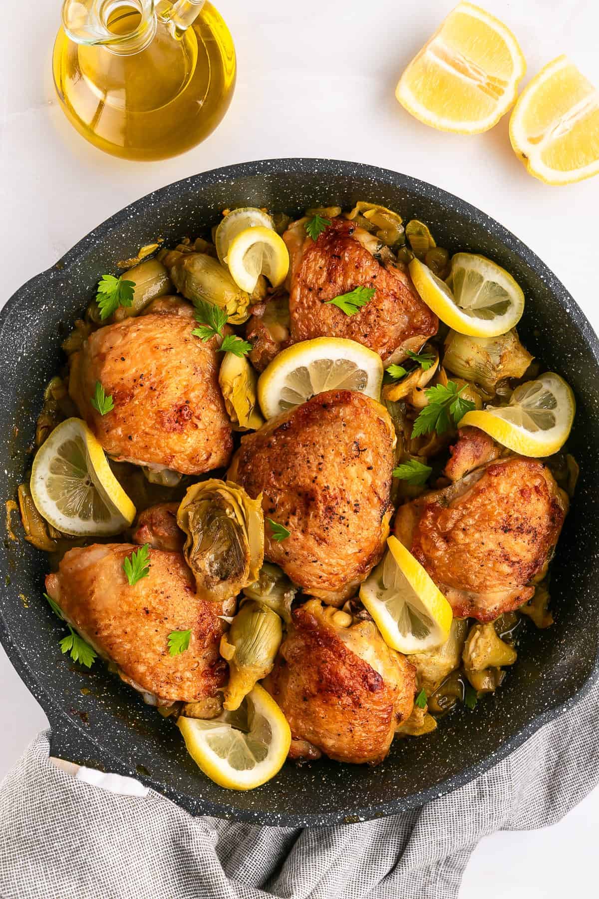 Artichoke chicken in a skillet with lemon slices.